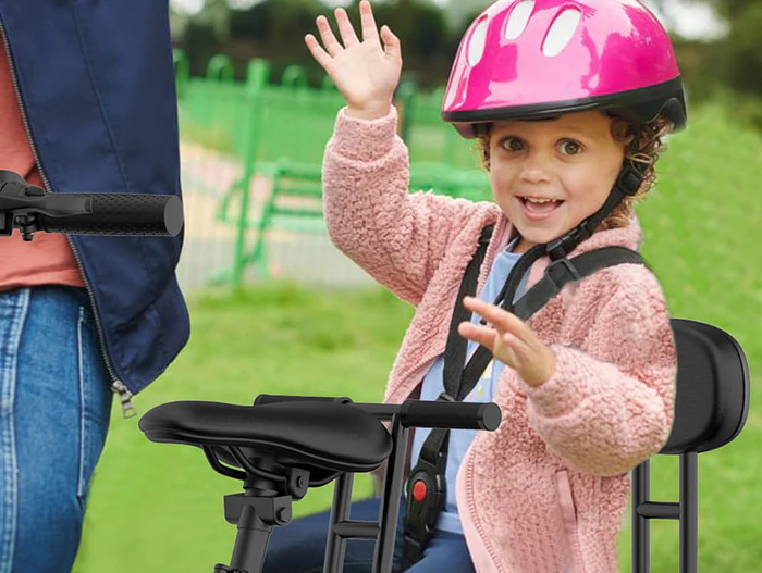 Happy child in pink helmet waves from e-bike front seat.