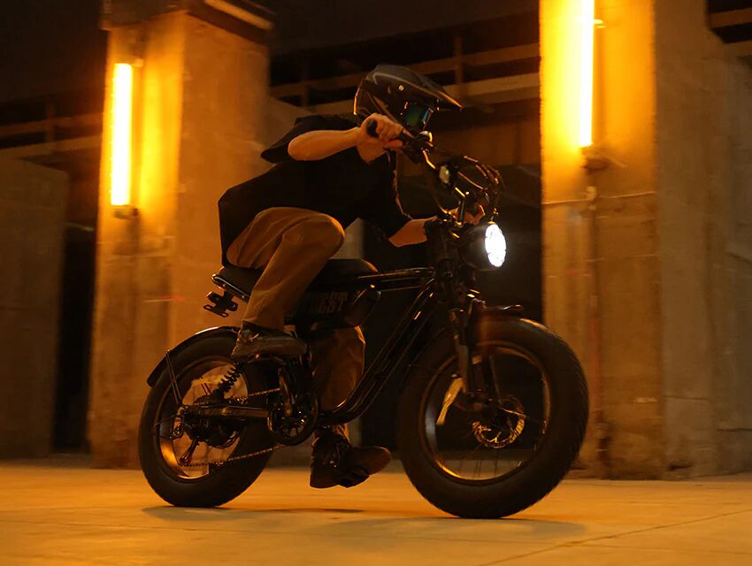 A person rides a moped-style electric bicycle at night.