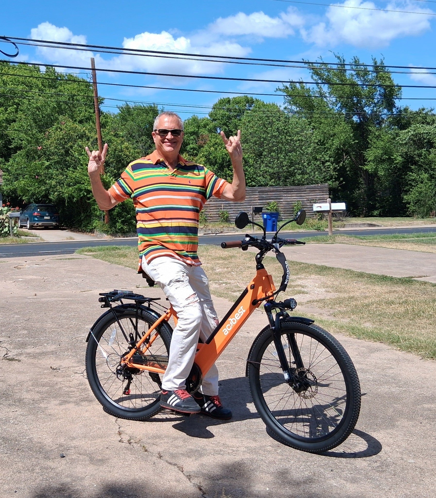 A smiling older man is sitting on an orange e-bike outdoors.