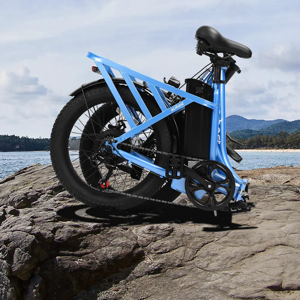 Folded blue Mars Electric Bike on rocks near a lake, showcasing fat tires.