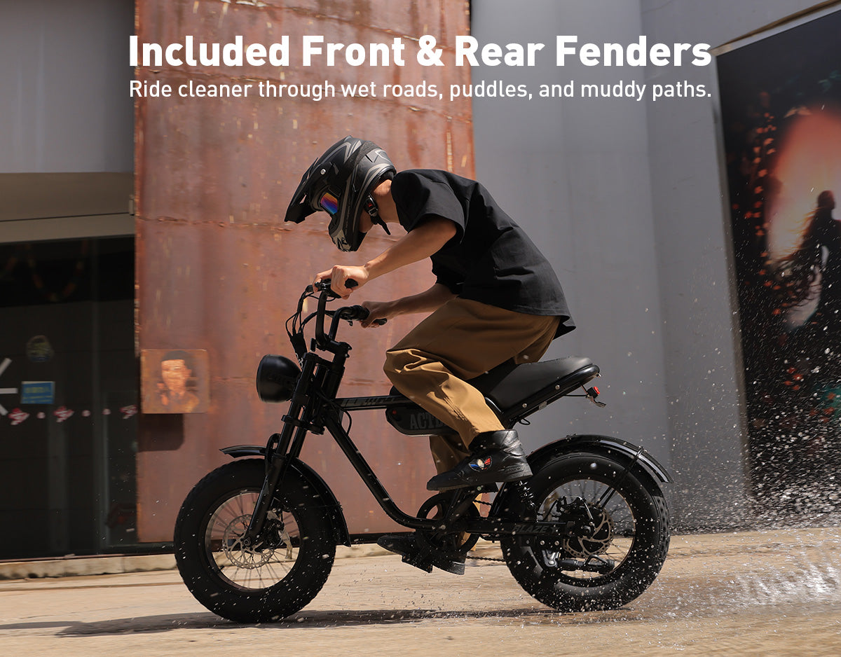 A person wearing a black helmet rides a black electric motorcycle outdoors, with large white text at the top reading 'Included Front & Rear Fenders' and smaller copy about riding cleaner through wet roads, puddles, and muddy paths.