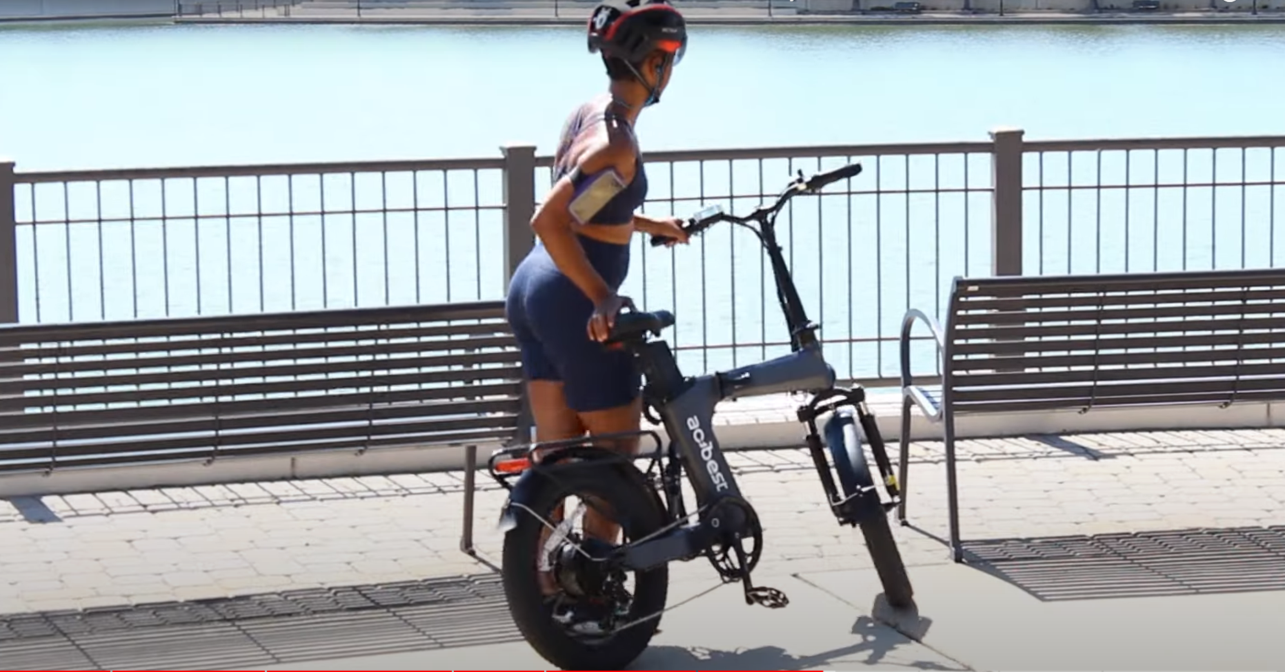 Woman wearing helmet walking a folding ebike on a waterfront path