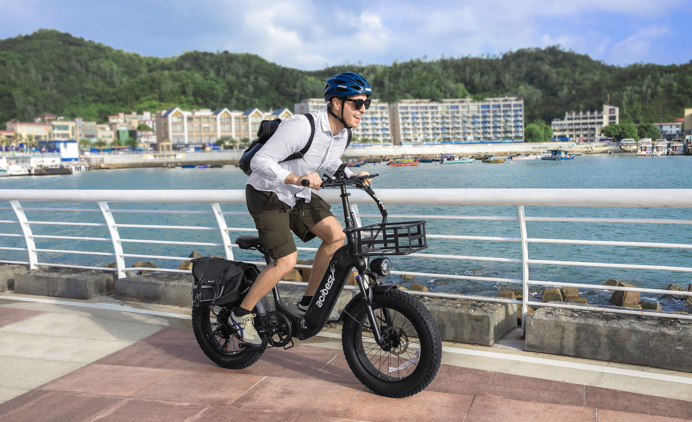 Man riding an Aostirmotor fat tire electric bike beside the waterfront with buildings in the background