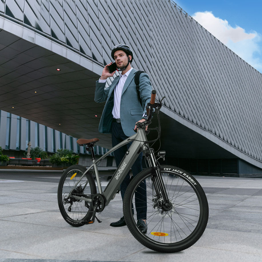 Man in suit on gray Core Mountain Electric Bike with brown seat at modern building.