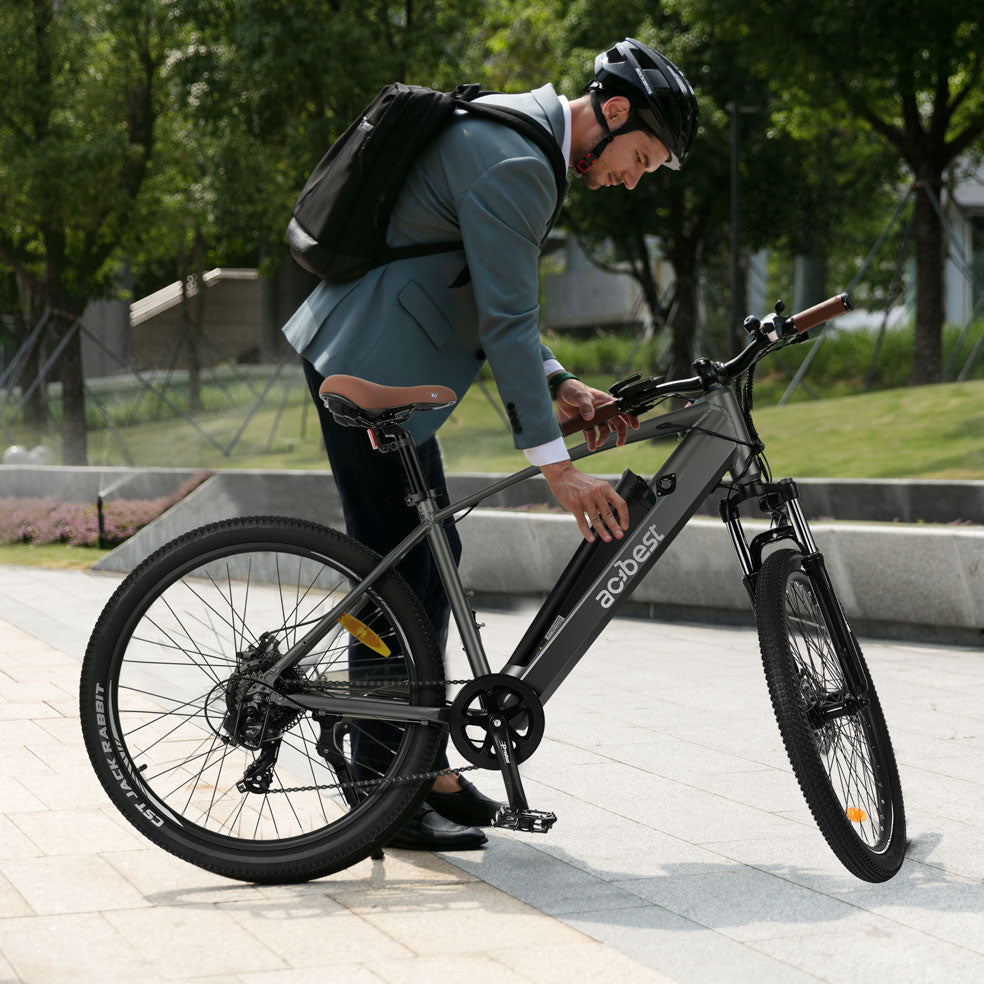Man in suit adjusting gray Core Mountain Electric Bike on city sidewalk.