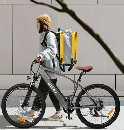 Woman walking with gray Core Mountain Electric Bike and a yellow backpack.