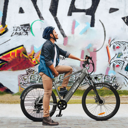Man smiling next to gray Core Mountain Electric Bike in front of colorful graffiti.