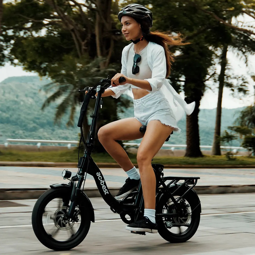 Woman riding black Actbest foldable electric bike in scenic outdoor location.