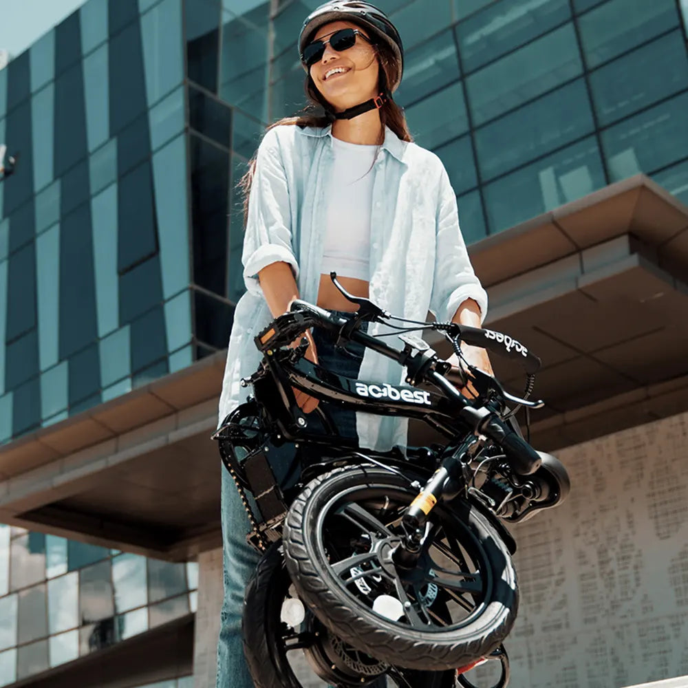 Woman carrying a folded black Actbest electric bike in urban environment.