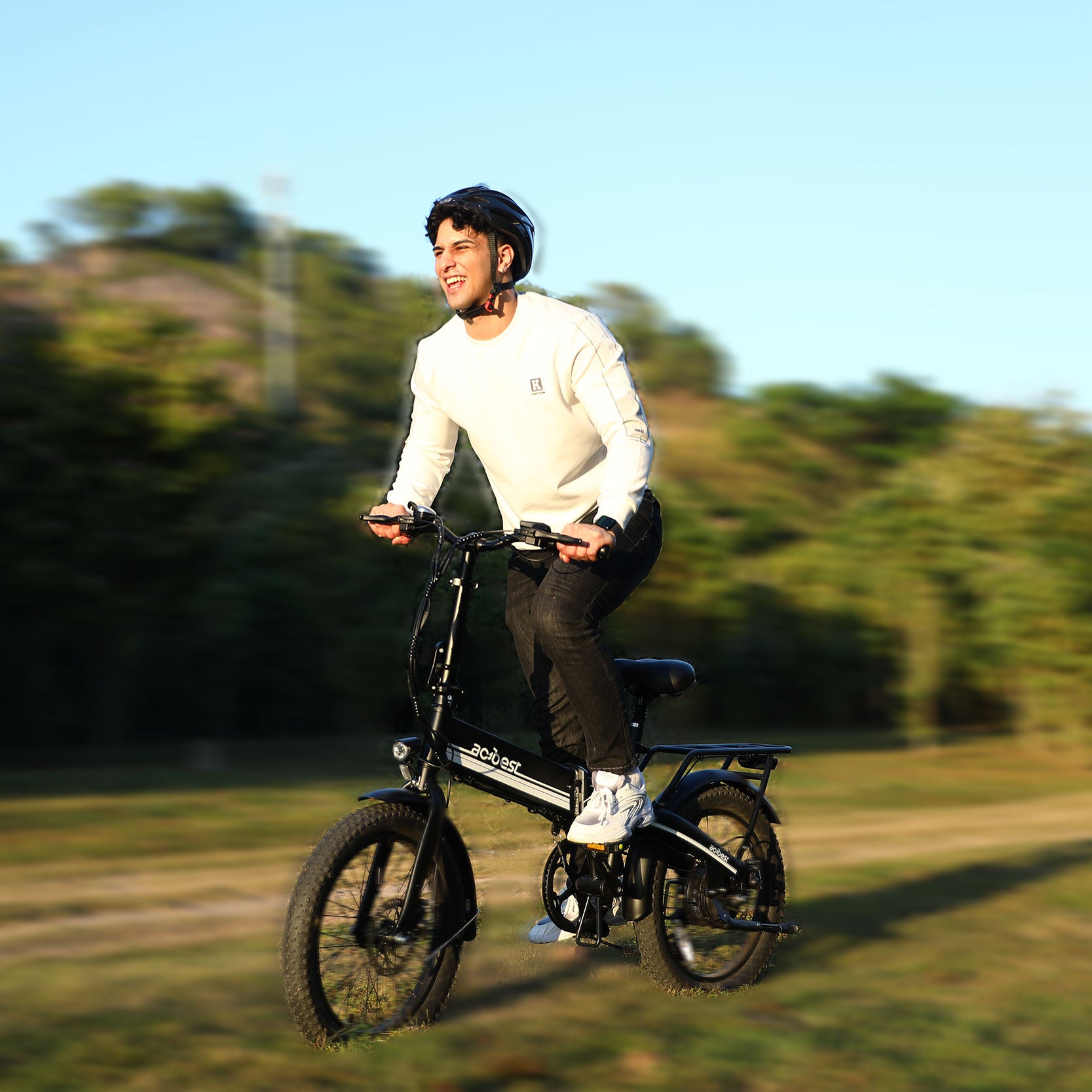 Man riding a black foldable electric bike with fat tires on a grassy trail.