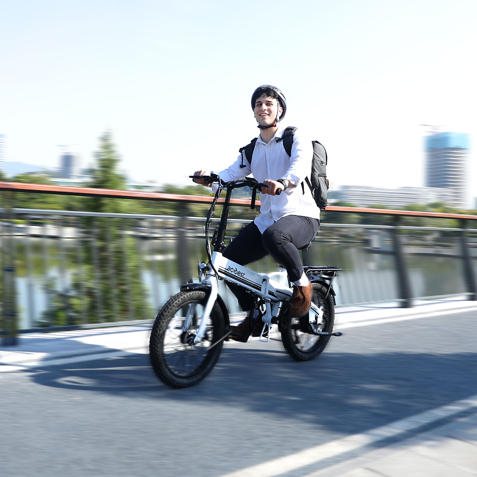 Man riding a white folding electric bike with fat tires on a city bridge.