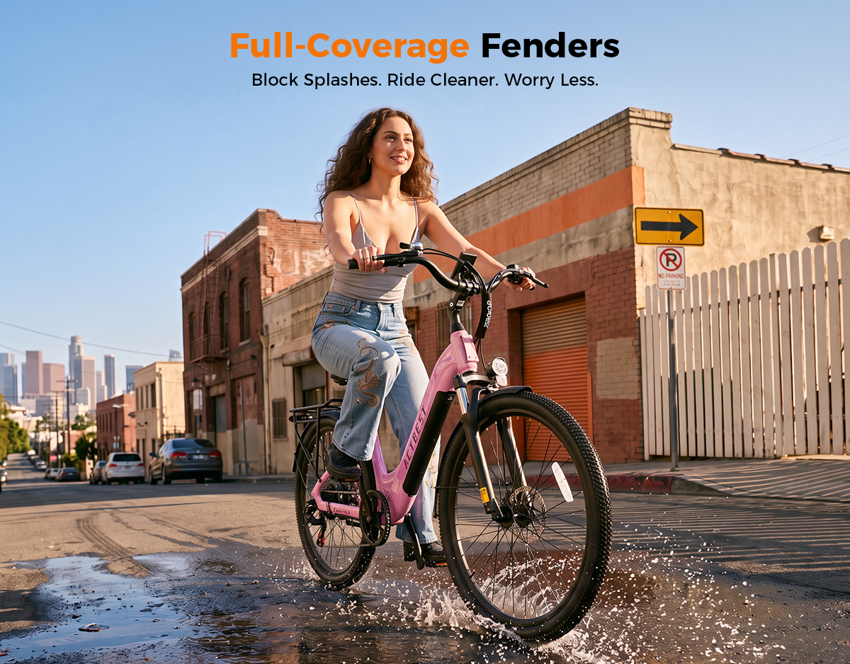 A woman rides a pink electric bicycle through a wet urban street puddle, with buildings, parked cars, and a city skyline in the background. Orange and black text at the top reads 'Full-Coverage Fenders' and 'Block Splashes.