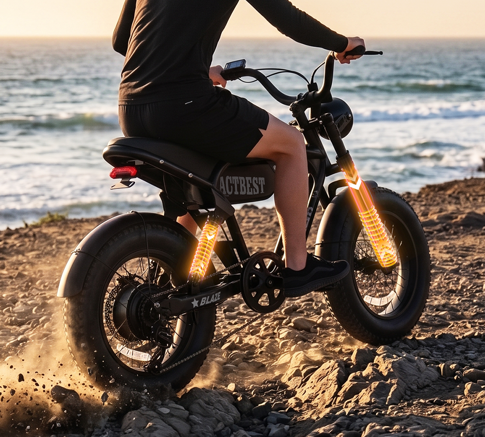 A person riding a black fat-tire electric bicycle on a rocky beach with the ocean in the background. The bike has glowing amber accent lights on the tires and a visible ACTBEST brand badge on the side panel.